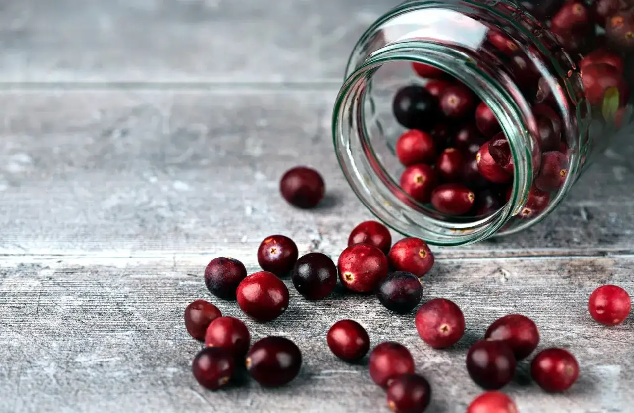 Des canneberges rouges et sombres débordent d'un bocal en verre renversé sur une surface en bois. Ces baies sont connues pour leurs nombreux canneberge bienfaits.