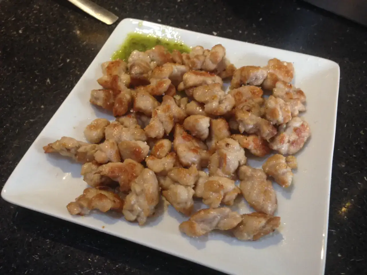 Deliciosas mollejas de cordero doradas, servidas en un plato blanco con una salsa verde.