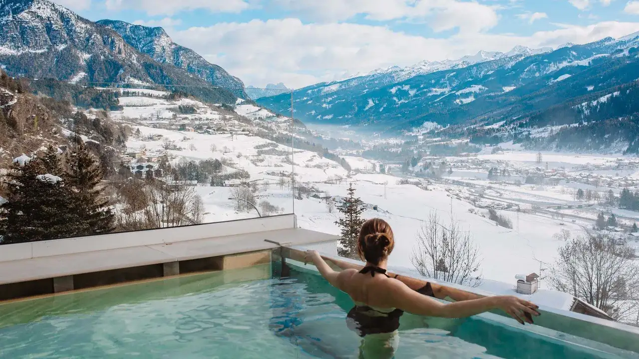 Donna rilassata in una piscina termale con vista su un paesaggio montano innevato, perfetta per una settimana bianca da sogno.