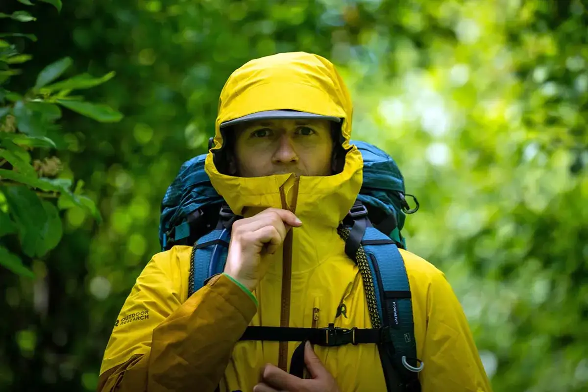 Mężczyzna w żółtej kurtce z kapturem i plecakiem, gotowy na wędrówkę. Czy lepszy będzie DryVent czy Gore-Tex?