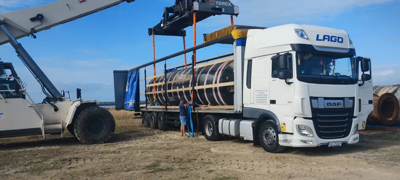 Ciężarówka LTL LAGO transportuje wielkogabarytowe elementy. Wózek widłowy podnosi ładunek, a pracownik zabezpiecza go pasami.