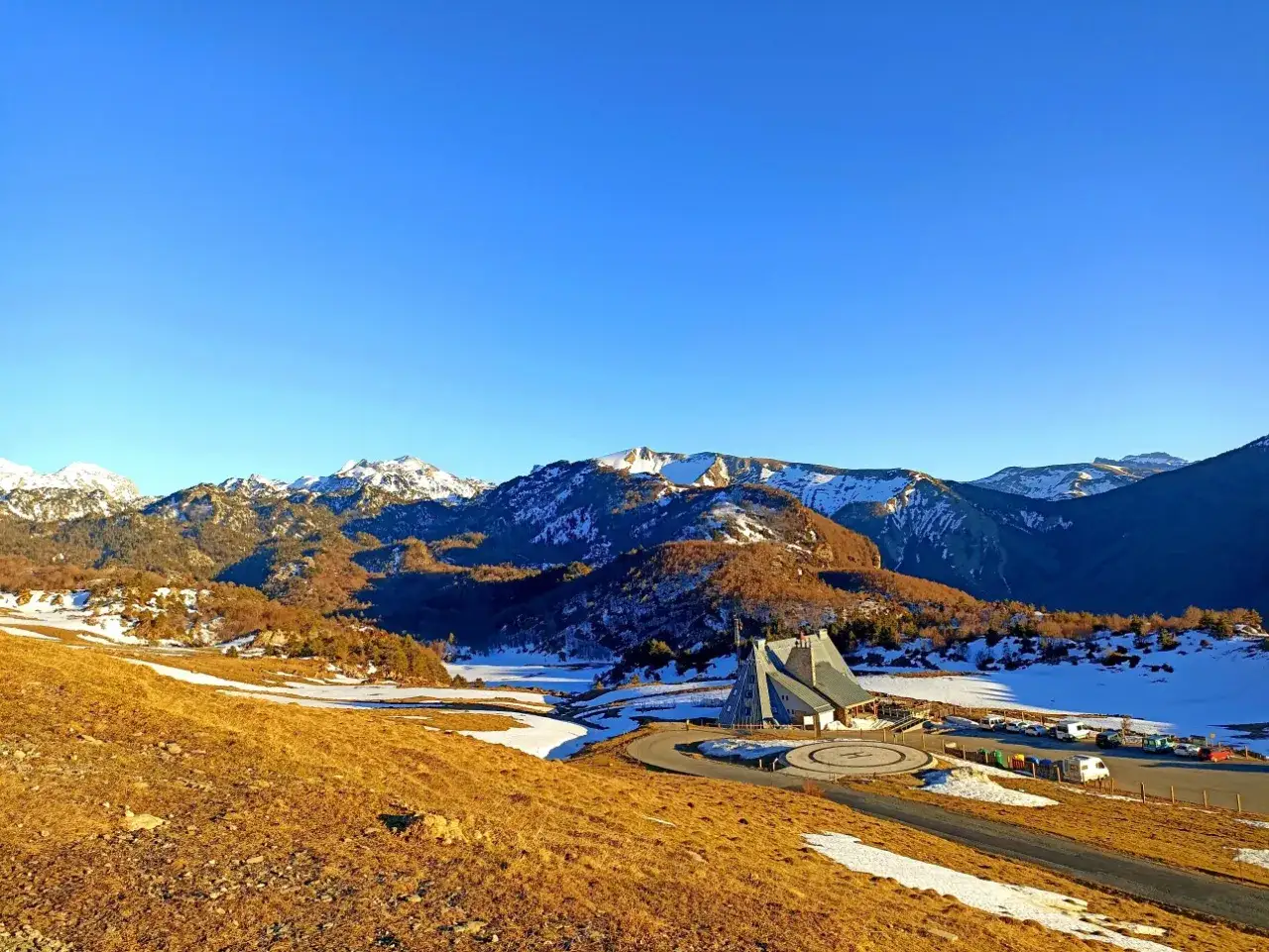 Paisaje invernal en el **valle de Belagua** con montañas nevadas, un edificio moderno y un aparcamiento.
