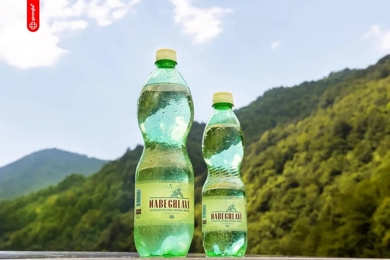 Dwie butelki Nabeghlavi, gruzińska woda mineralna, na tle zielonych gór.