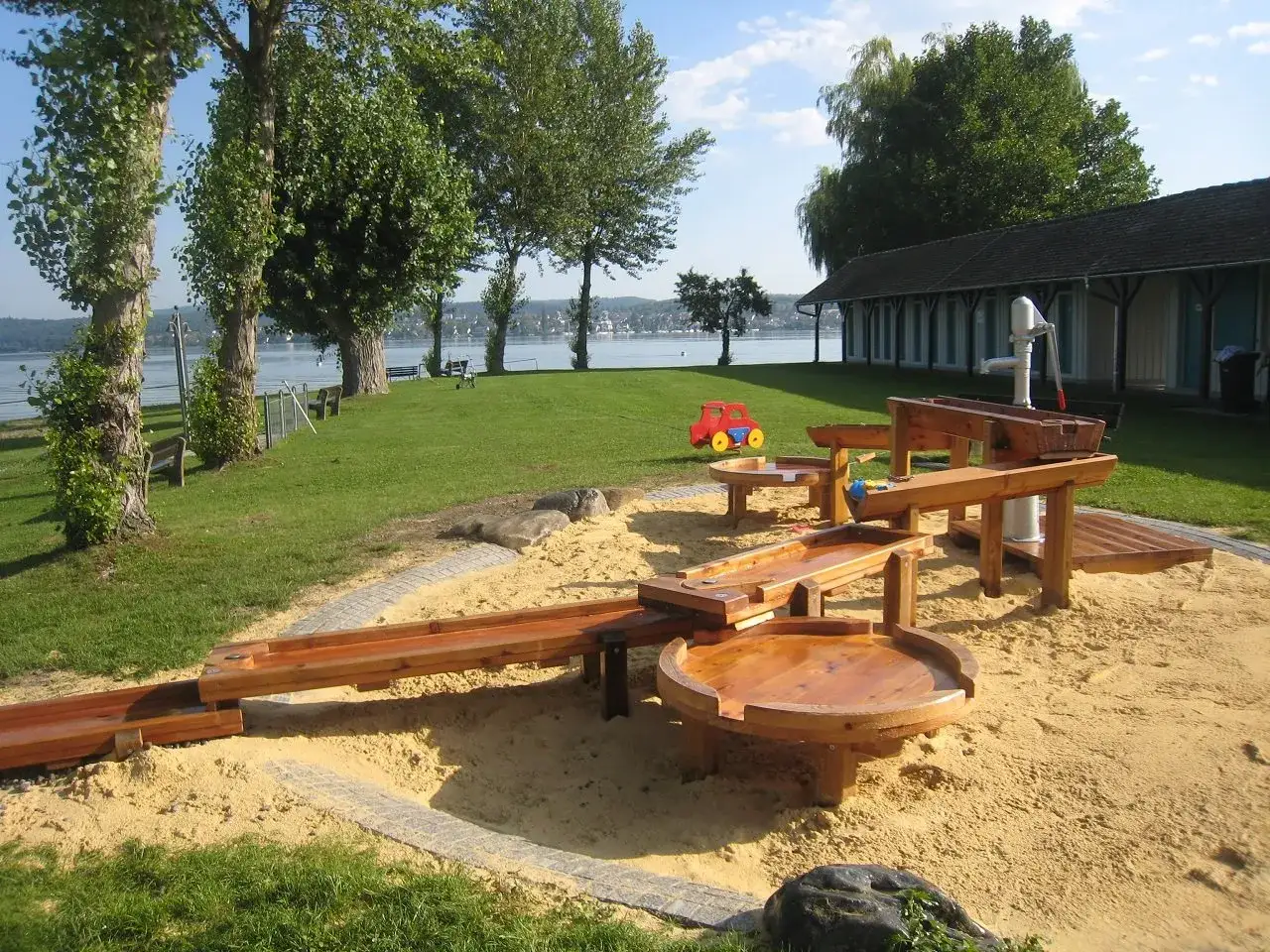 Wasserspielplatz auf der Insel Reichenau mit Holzelementen und Sand. Kinder planschen im Wasser, w&auml;hrend die Sonne scheint.