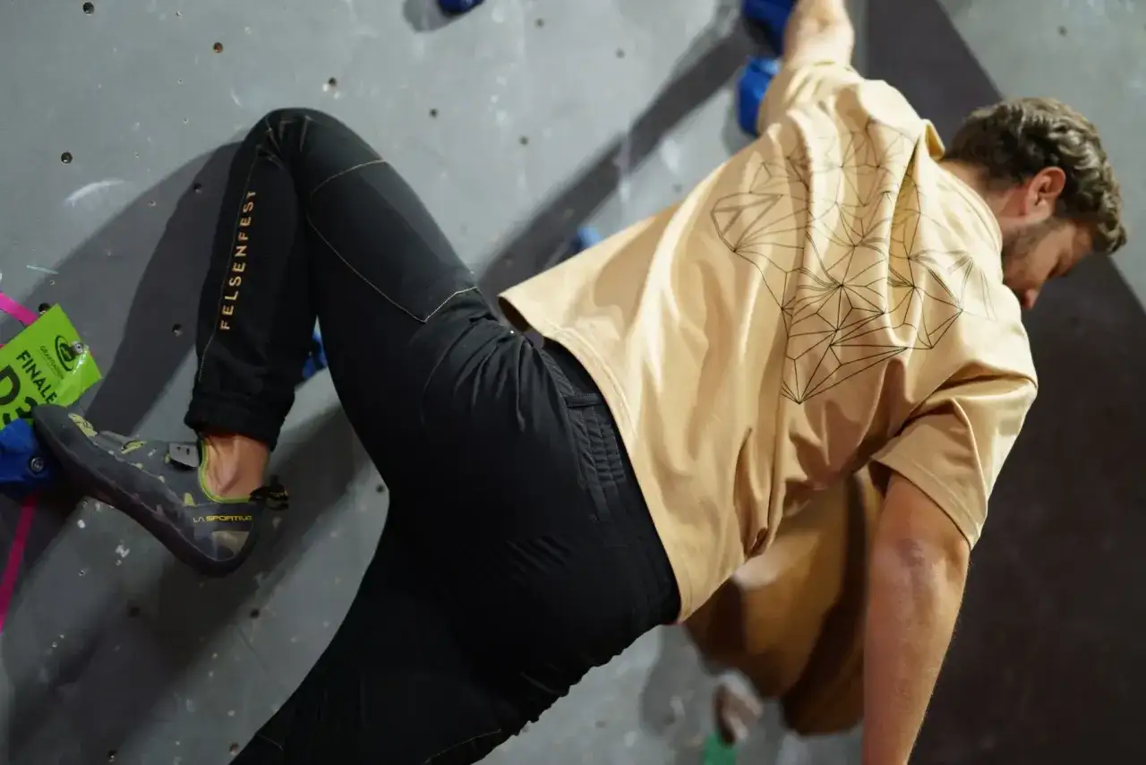 Mann in beiger Shirt und schwarzer Hose beim Bouldern. So zieht man zum Bouldern an: bequeme Kleidung f&uuml;r maximale Bewegungsfreiheit.