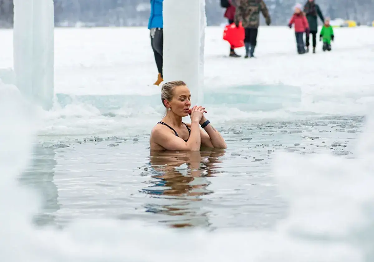 Kvinna tar ett isbad i en isvak. Vattenytan är täckt av isbitar. I bakgrunden syns snö och is.