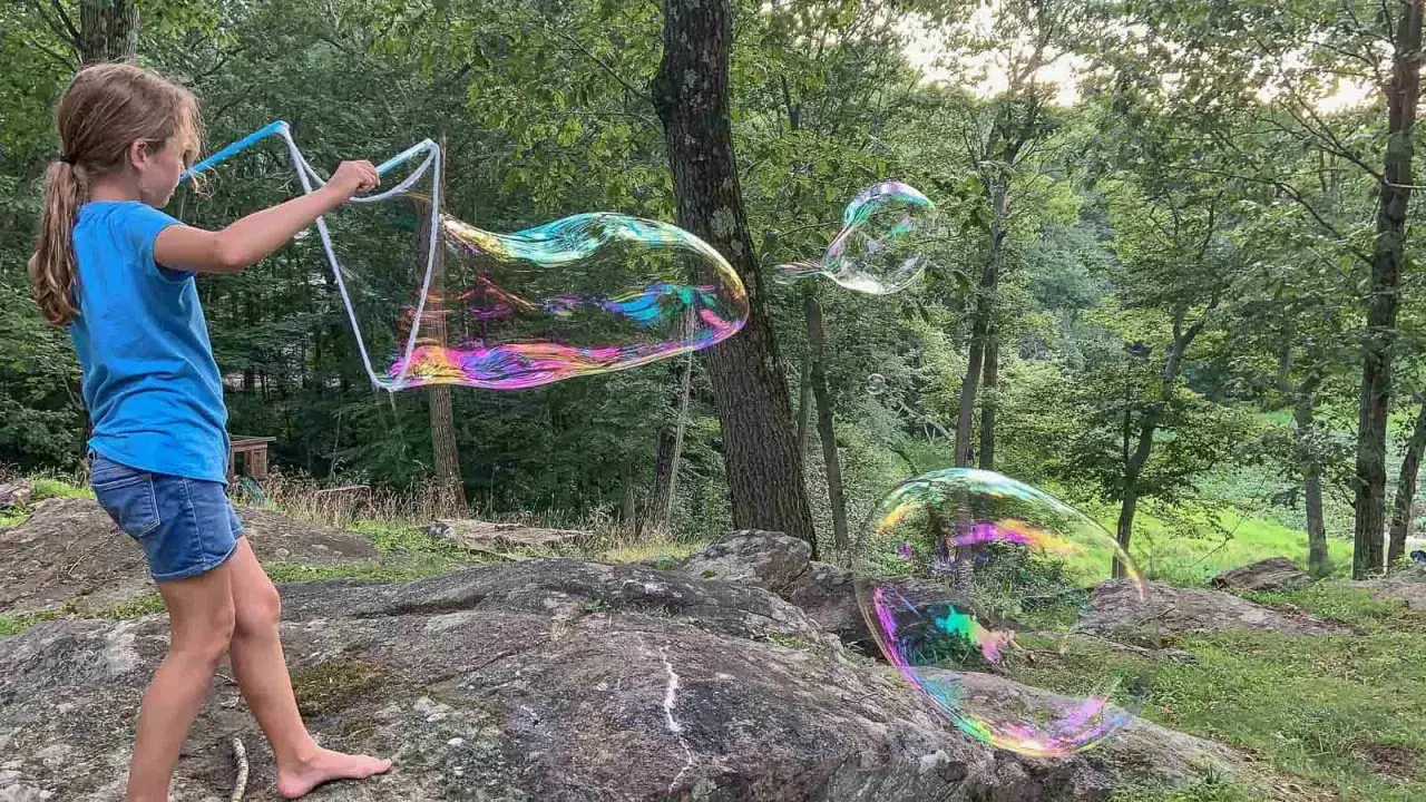 Ein M&auml;dchen macht im Wald mit einem gro&szlig;en Ring riesige, schillernde Seifenblasen. Ein toller Nachmittag, um Seifenblasen selber zu machen!