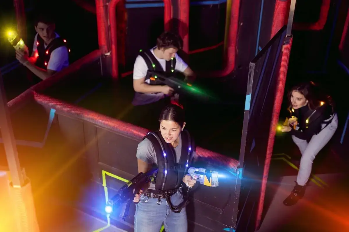 Vier junge Leute spielen **underground lasergame Berlin**. Sie tragen Westen mit Lichtern und halten Lasergewehre in der Hand, w&auml;hrend sie sich in der dunklen Arena bewegen.