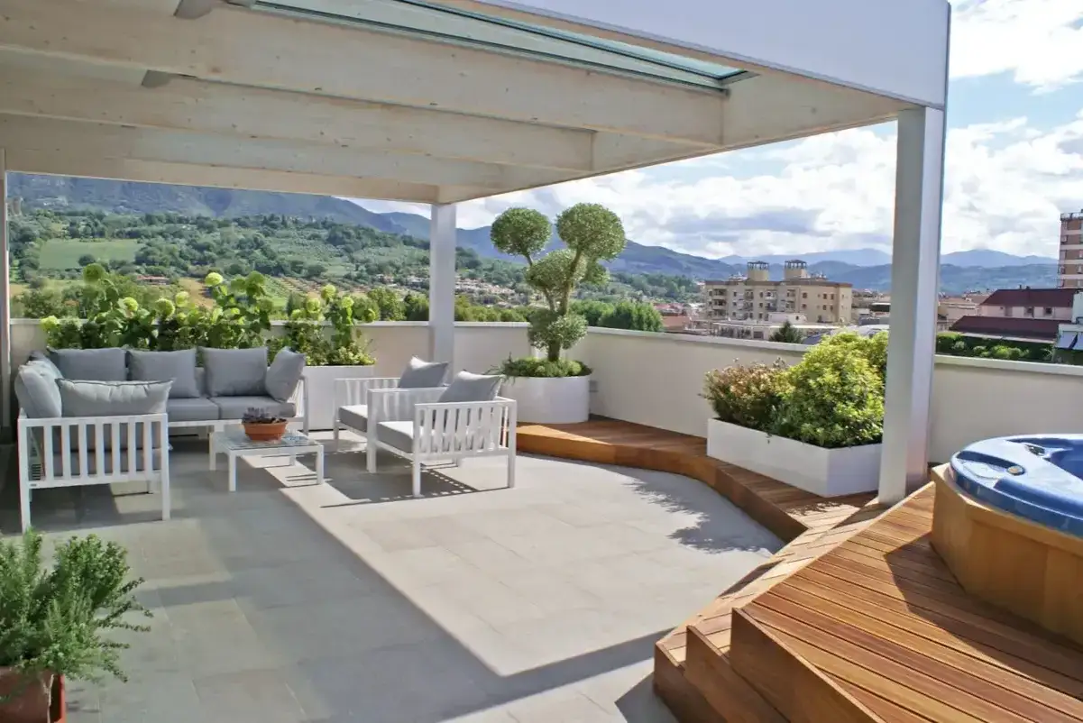 Un elegante progetto terrazzo attico con arredi bianchi, vasca idromassaggio e vista panoramica sulle colline.