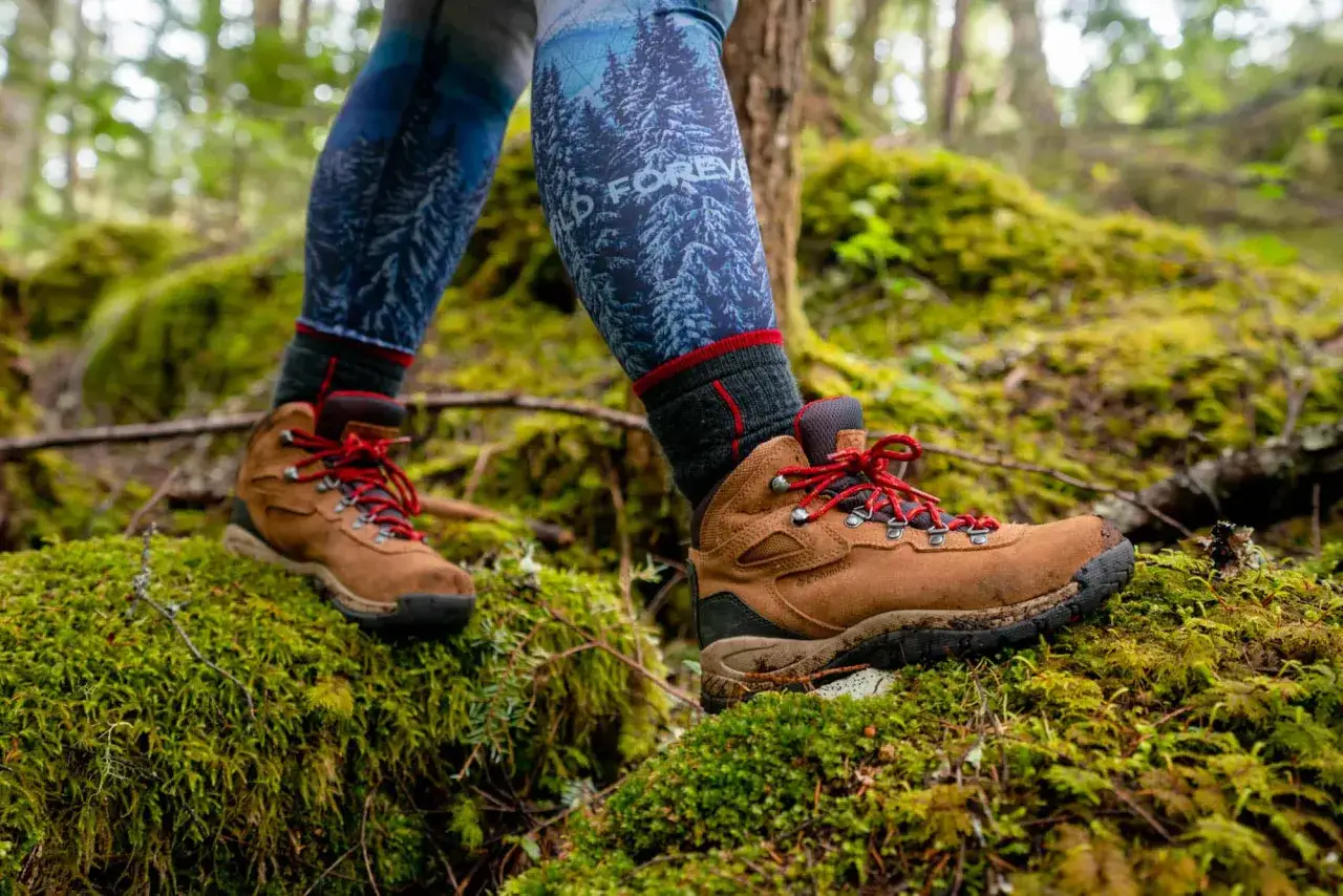 Hiking through a mossy forest, the wearer's boots are slightly too big, but the red laces add a pop of color against the earthy tones.