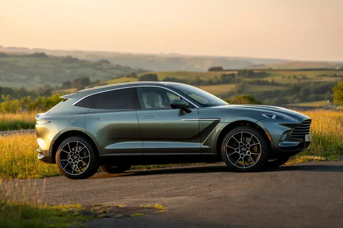 Zielony Aston Martin DBX na tle malowniczego krajobrazu o zachodzie słońca.