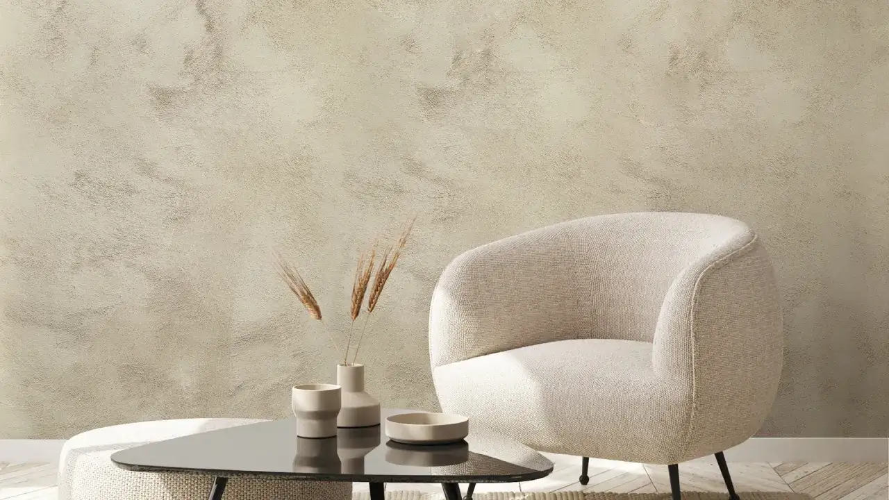 Un fauteuil confortable et une table basse avec des vases et des épis de blé devant un mur texturé avec un enduit décoratif.