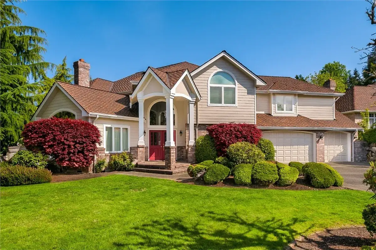 A beautiful home with a well-maintained lawn and vibrant red bushes. The asphalt roof looks good, complementing the house's architecture.