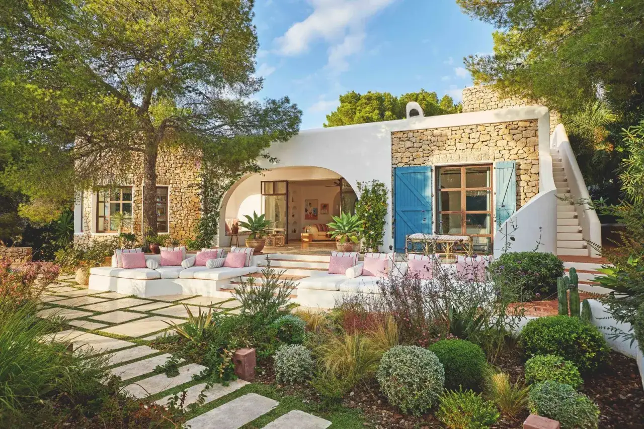 Un oasis de paz con jardines bonitos, sofás blancos y almohadas rosas bajo un árbol frondoso.