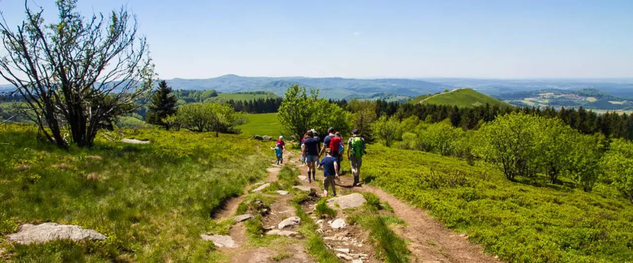 Familie genießt das Wasserkuppe wandern auf einem sonnigen Bergpfad mit weiten Ausblicken über grüne Hügel und Wälder.