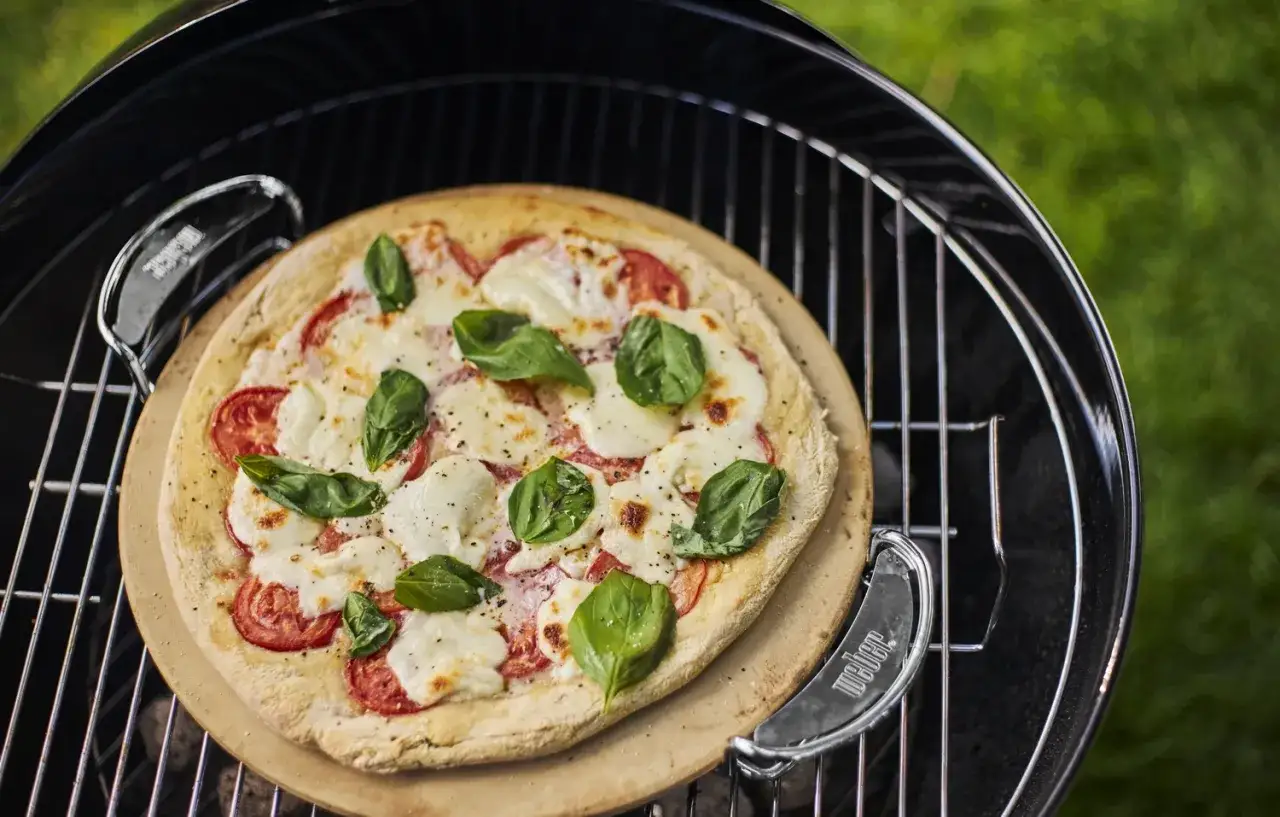 Pieczenie pizzy na kamieniu w grillu. Gorąca Margherita z pomidorami, mozzarellą i bazylią nabiera smaku.