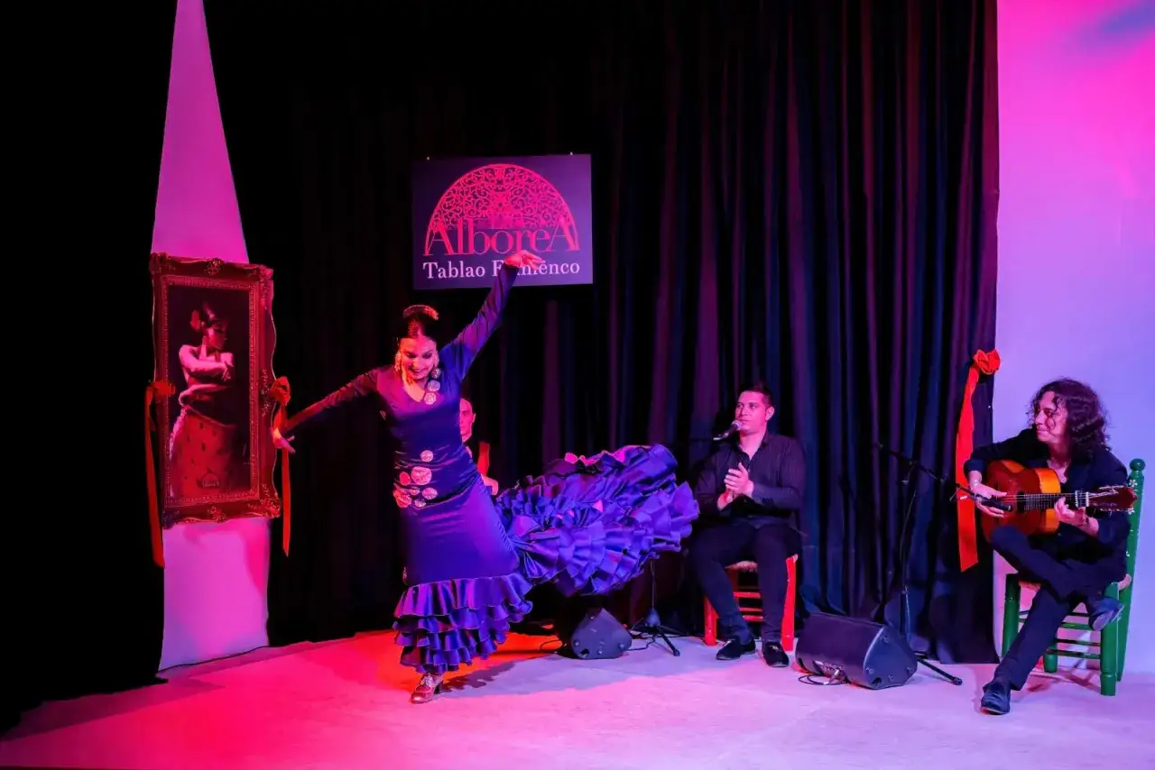 Artistas flamencos de Granada en pleno espect&aacute;culo. Una bailaora con un vestido morado despliega su falda mientras un cantaor y un guitarrista la acompa&ntilde;an.