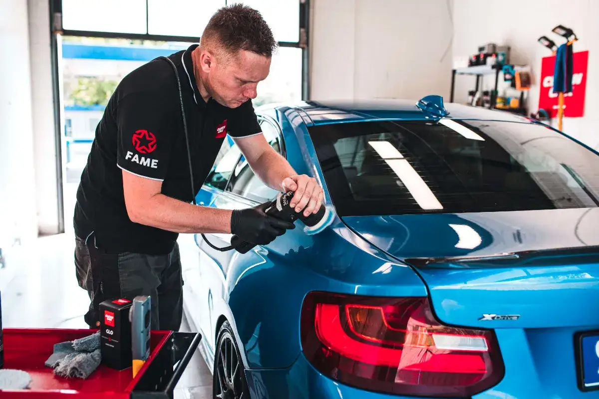 Profesjonalista wykonuje naprawę lakieru bezbarwnego niebieskiego BMW, polerując karoserię maszyną.