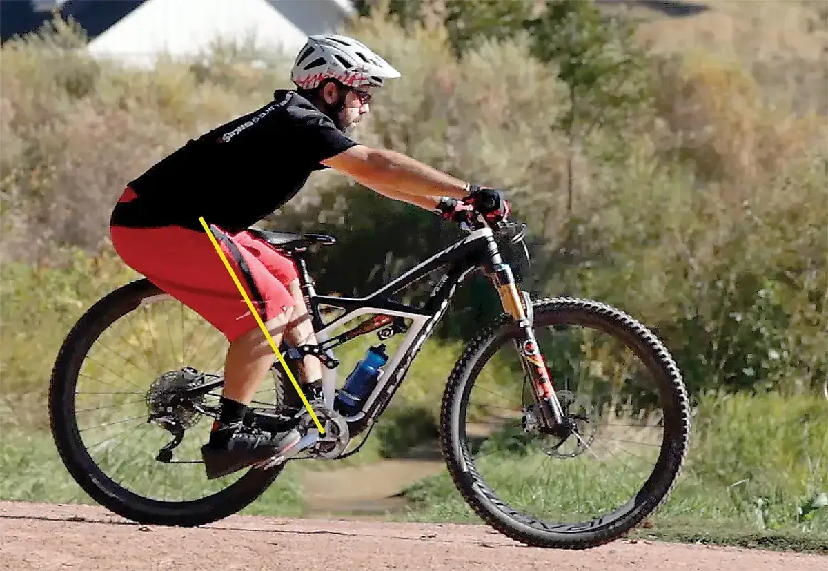 A cyclist demonstrates proper body position for how to brake on a bike, leaning back slightly with weight over the rear wheel.