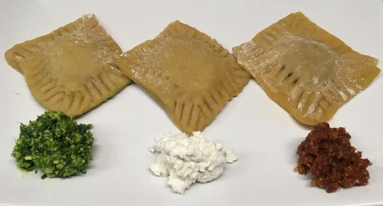 Drei quadratische Ravioli mit Rillenrand, daneben Pesto, Ricotta und getrocknete Tomaten. Ein italienisches ravioli-teig rezept zum Genießen.