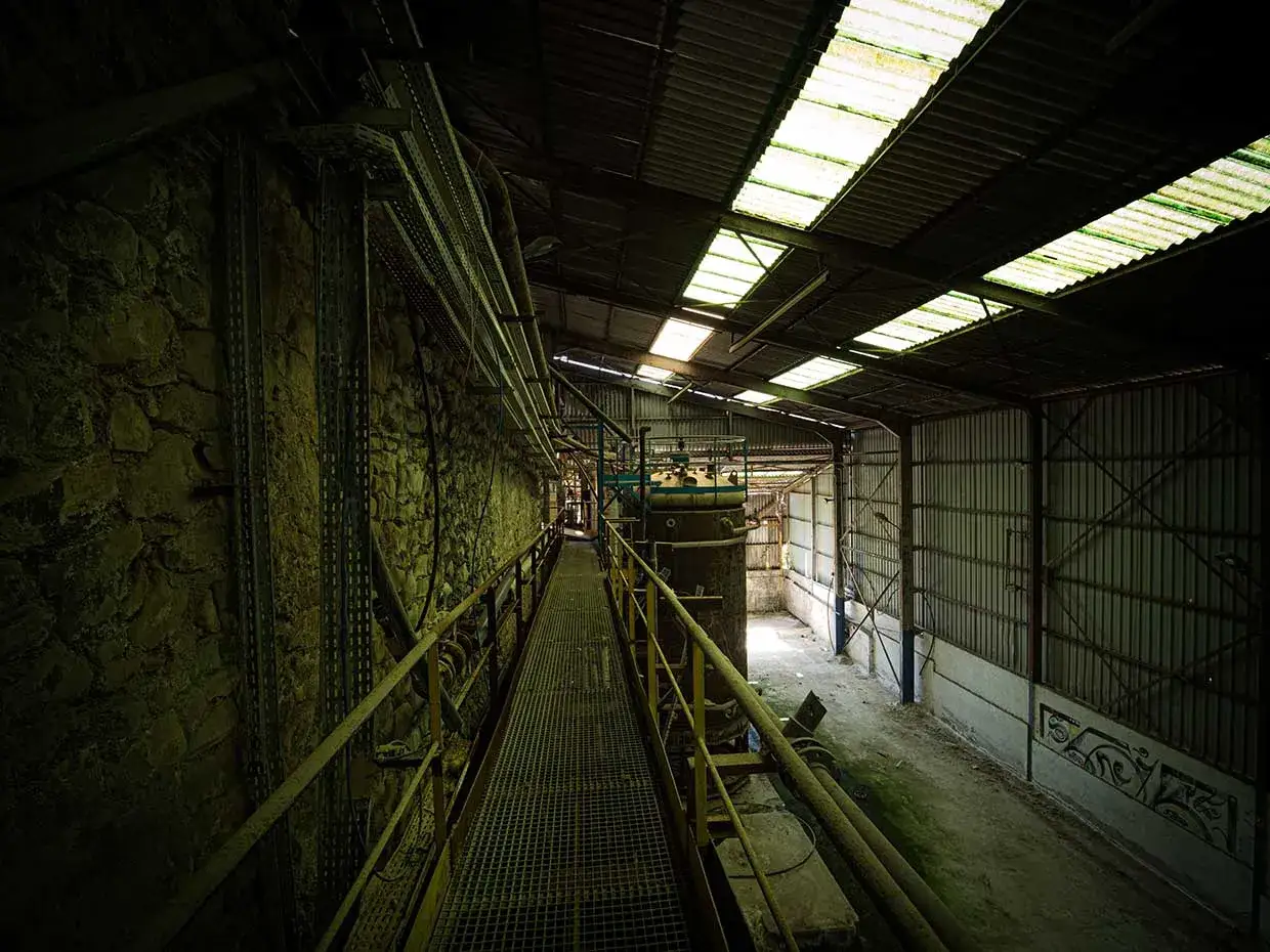 Passerelle rouillée dans une usine abandonnée, parfaite pour faire de l'urbex. Lumière filtrant par le toit, ambiance industrielle.
