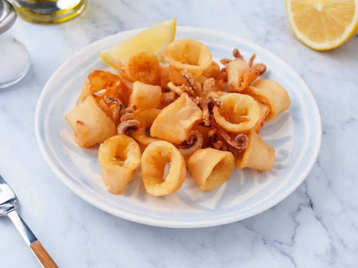 Crujientes chipirones fritos en un plato, acompa&ntilde;ados de un gajo de lim&oacute;n y un salero.