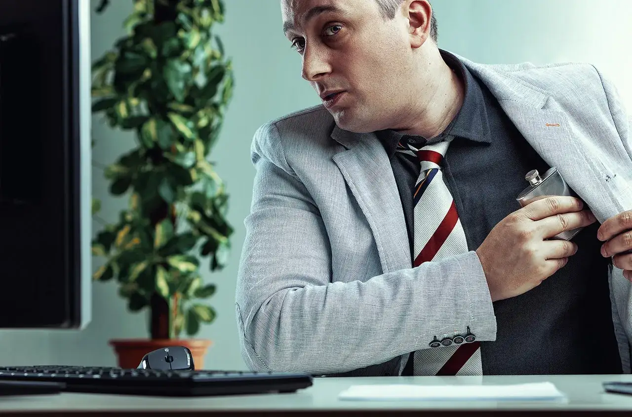 Mężczyzna w garniturze chowa piersiówkę do kieszeni. Czy barman może pić w pracy? To pytanie pozostaje otwarte.