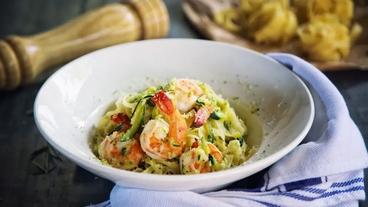 Un piatto invitante di pasta con zucchine e gamberetti, guarnito con scorza di limone grattugiata.