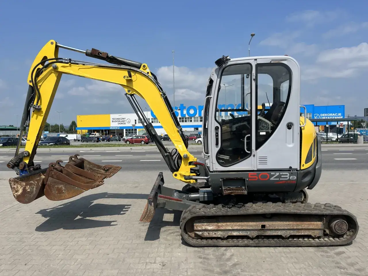 Żółto-szara minikoparka Wacker Neuson 50Z3e z gąsienicami stoi na chodniku.