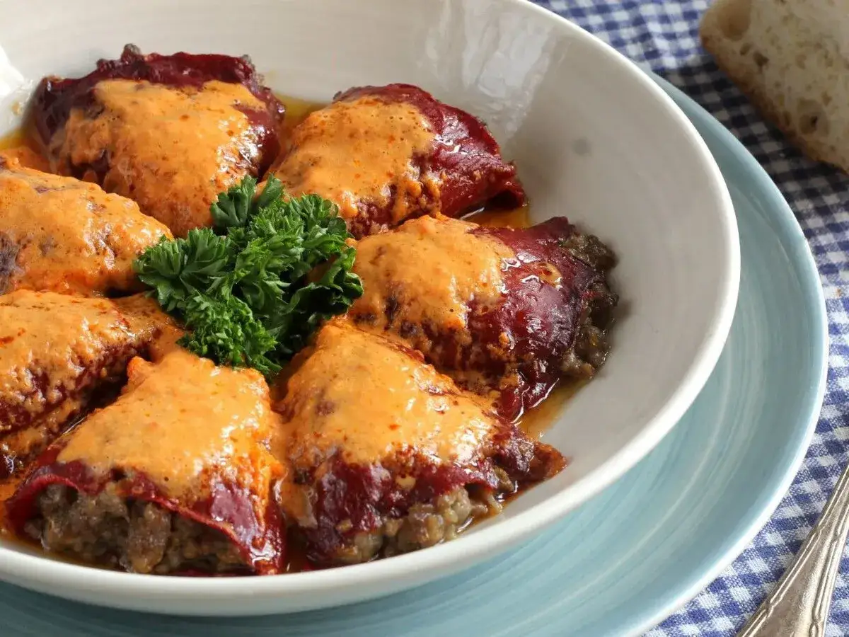 Pimientos rellenos de carne cubiertos con una cremosa salsa naranja, adornados con perejil fresco.