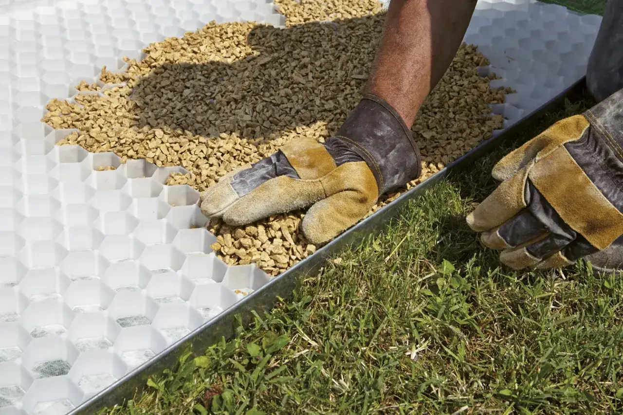 Mani guantate spargono ghiaia su una griglia per creare un vialetto giardino ghiaia stabile.