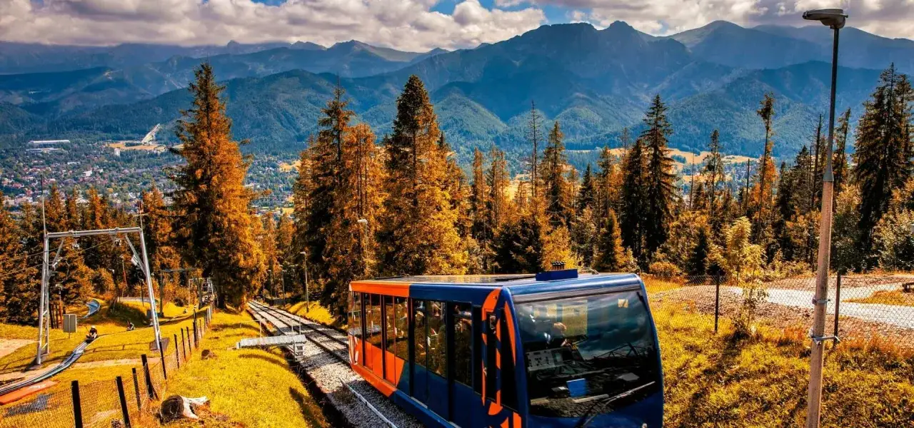 Kolejka linowo-terenowa wjeżdża na Gubałówkę, oferując widok na jesienne drzewa i Tatry.