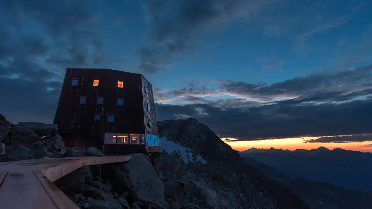 Il rifugio Sasso Nero, con le sue luci accese, si staglia su un paesaggio montano al tramonto.