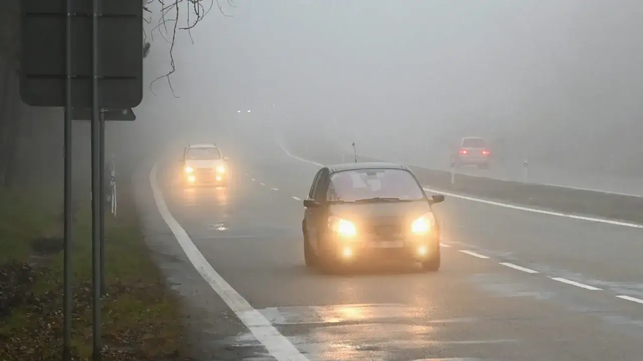Mglisty poranek na drodze. Samochody jadą ostrożnie, włączone światła przeciwmgielne przebijają się przez gęstą mgłę, poprawiając widoczność.