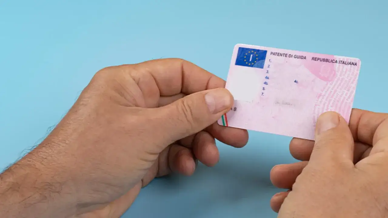 Mani che tengono una patente di guida italiana. Si parla di assicurazione auto senza patente, ma la patente è fondamentale.