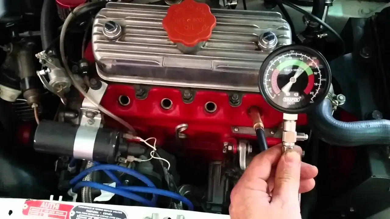 Mano sujetando un compresimetro conectado a un motor. El man&oacute;metro indica la presi&oacute;n de compresi&oacute;n.
