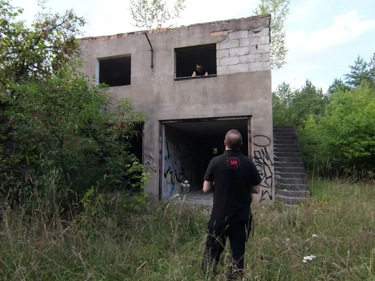 Mężczyzna stoi przed opuszczonym budynkiem, który może być najbardziej nawiedzonym domem w Polsce. W oknie na piętrze widać postać.