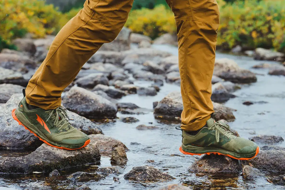 Zielone buty trekkingowe z pomarańczową podeszwą, idealne na wędrówki po kamienistym strumieniu. To buty, w których noga się nie poci, zapewniając komfort nawet w trudnych warunkach.