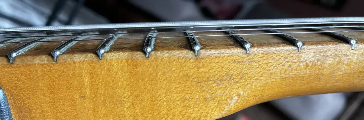 Nahaufnahme des Halses einer E-Gitarre mit Saiten und Bundst&auml;bchen. Das Holz hat eine warme, honigfarbene Maserung.