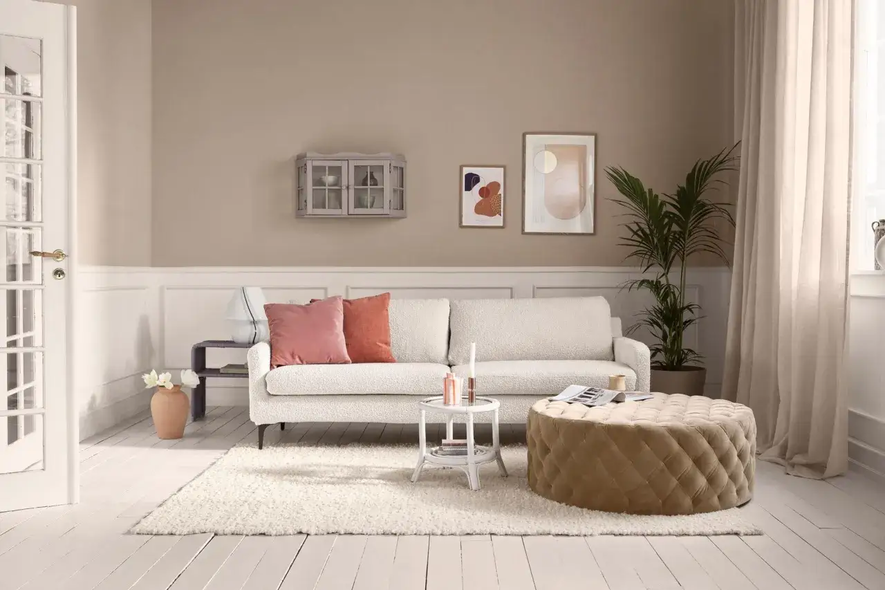 Gemütliches Wohnzimmer mit beiger Wirkung: weißes Sofa, Stepphocker, Teppich und Wandfarbe schaffen eine warme Atmosphäre.