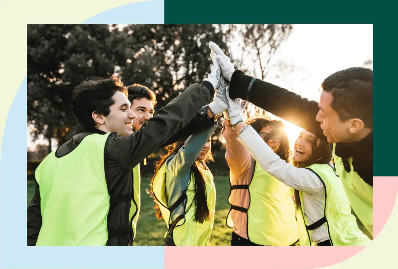 A diverse group of young people in bright vests give a high five, celebrating their participation in volunteer programs for youth.