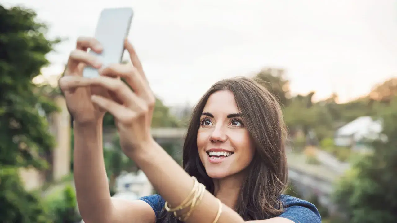 Mujer sonriente se toma un selfie con su m&oacute;vil. Aprende como hacer un selfie con el m&oacute;vil y captura tus mejores momentos.