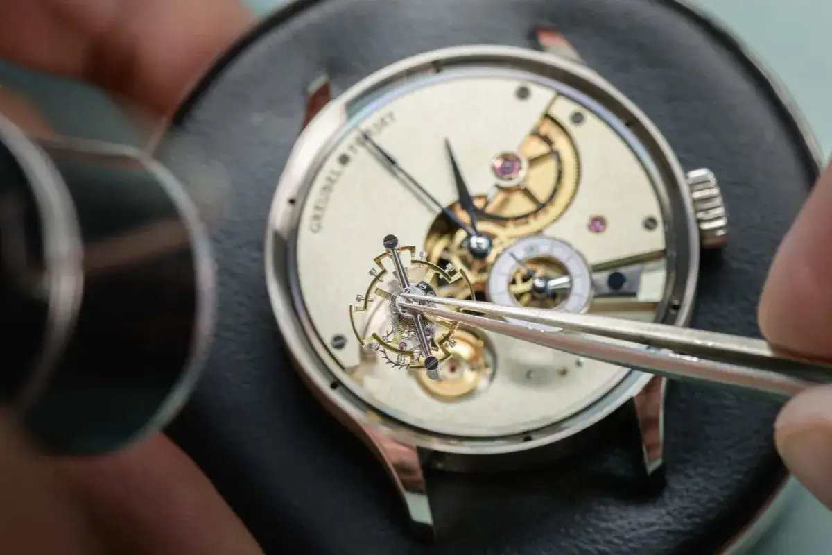 Un horloger assemble un mouvement complexe, démontrant son expertise montre. Les rouages dorés et les minuscules composants révèlent un savoir-faire exceptionnel.