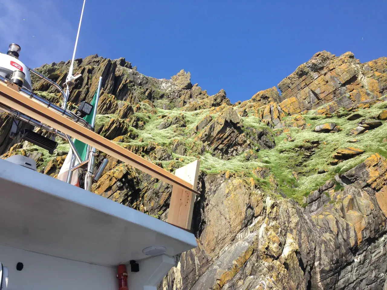 Łódź przy skalistym wybrzeżu, zielona roślinność. Planowanie logistyki trasy na wyspę Skellig Michael wymaga uwzględnienia pogody i fal.