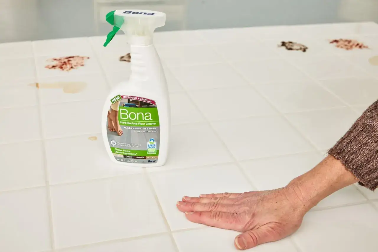 Une main nettoie du carrelage tach&eacute; avec le meilleur produit pour faire briller le carrelage, le nettoyant Bona.