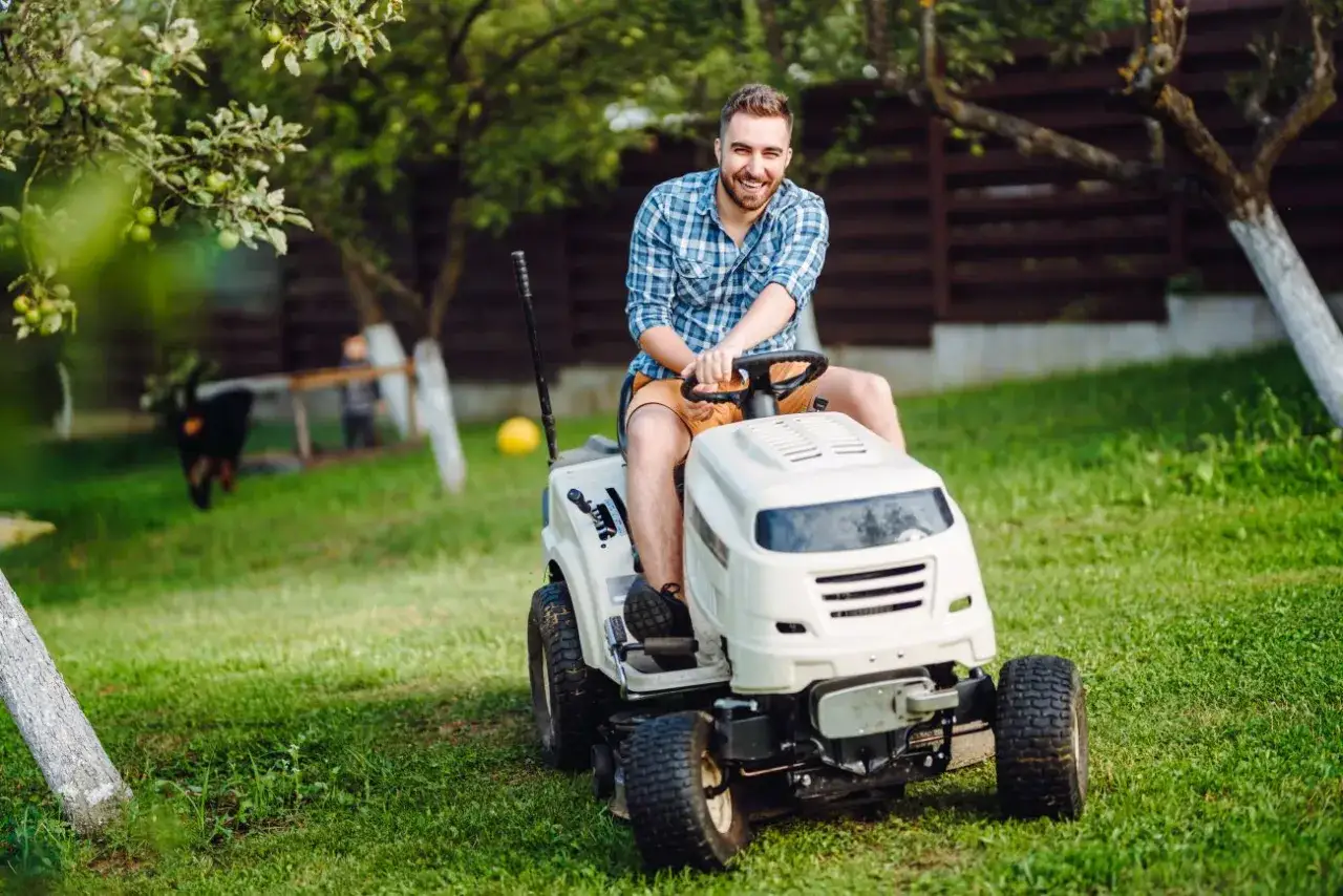 Uśmiechnięty mężczyzna na białej kosiarce do traktorka, gotowy do pracy w ogrodzie.