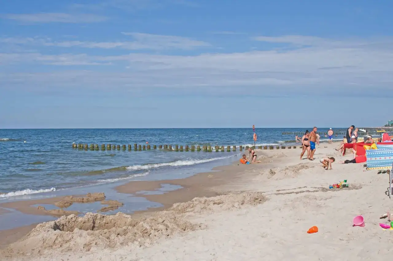 Słoneczny dzień na plaży w Dziwnowie nad morzem. Ludzie odpoczywają, dzieci budują zamki z piasku.