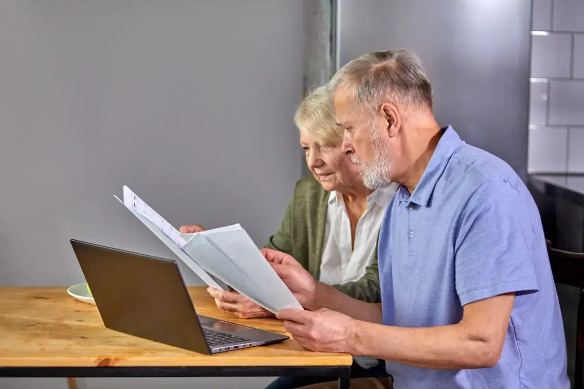 Starsza para przegląda dokumenty przy laptopie, analizując swoje przywileje emeryta.