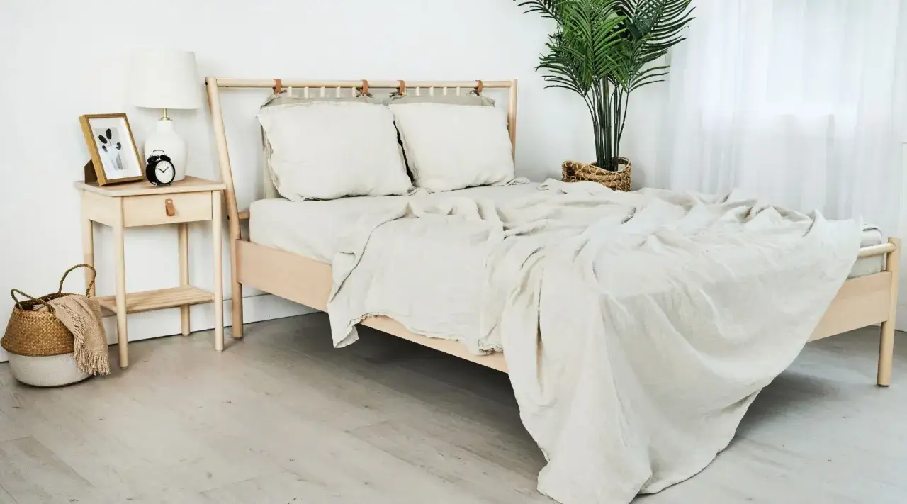 Camera da letto scandinava in stile nordico con letto in legno chiaro, biancheria beige e comodino con lampada e sveglia.