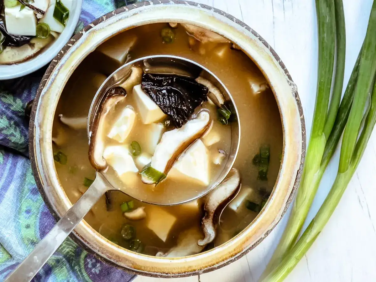 Aksamitna zupa miso z tofu, grzybami shiitake i szczypiorkiem, podana w glinianej misie.